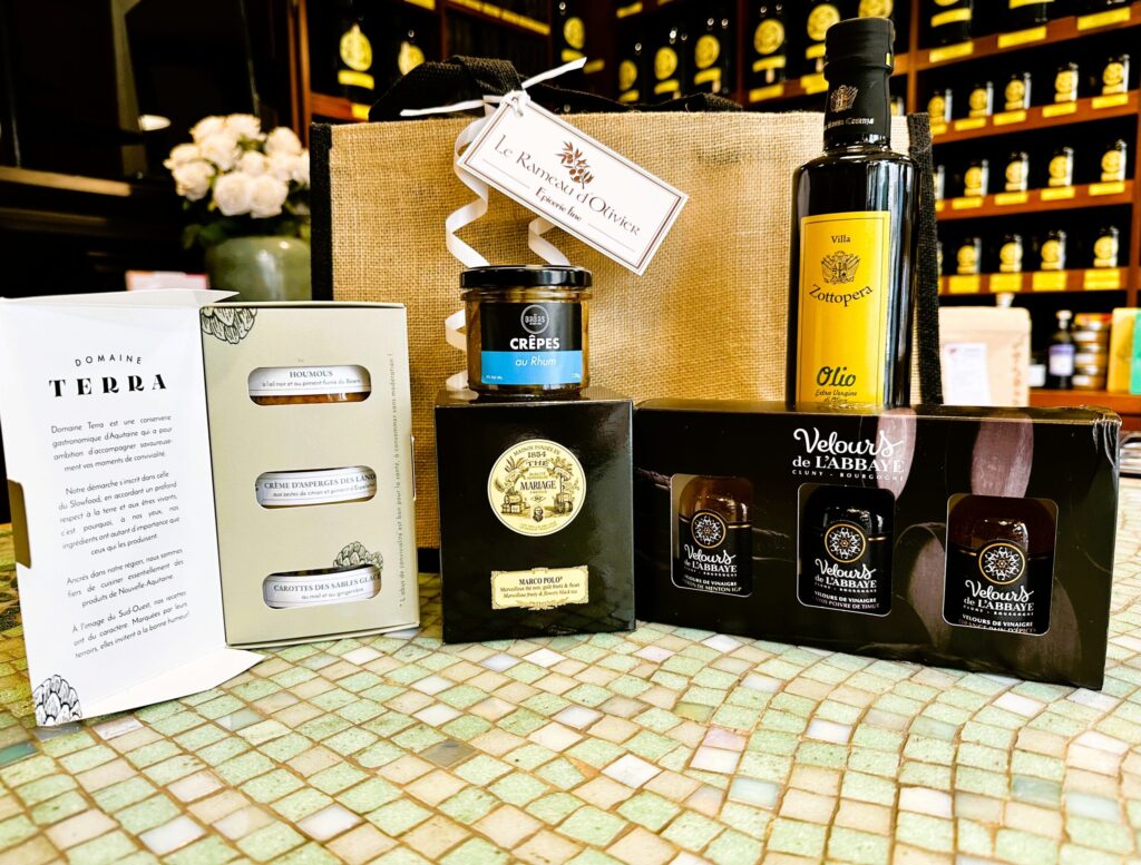 Une Sélection Escapade Gourmande avec huile d'olive, thé Mariage Frères, coffret Velours de l'Abbaye, coffret Domaine Terra et mini-crèpes au rhum dans un élégant sac en jute